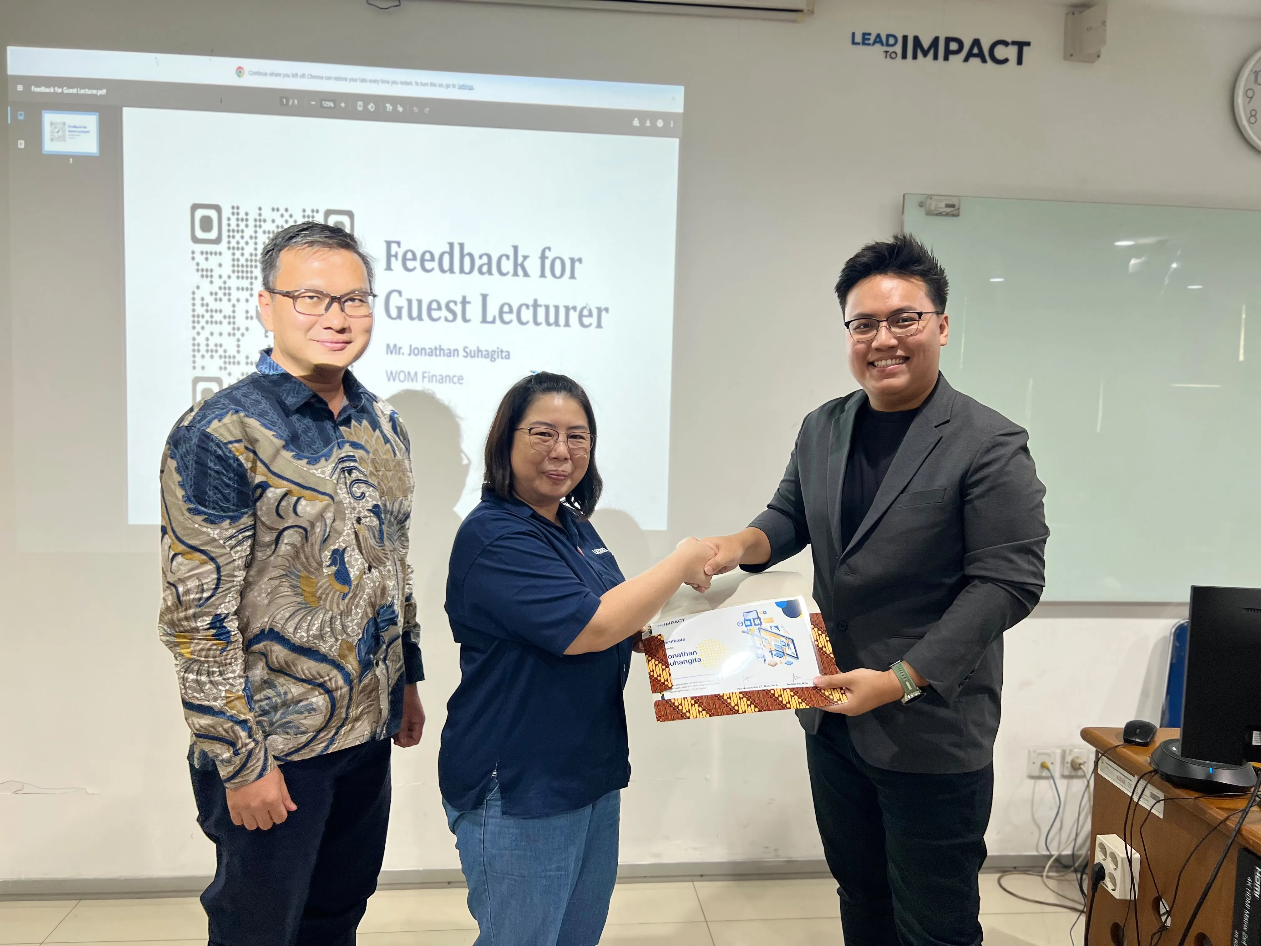 Jonathan Suhangita receiving a guest lecturer certificate at UKRIDA, in front of a slide thanking him for the WOM Finance session